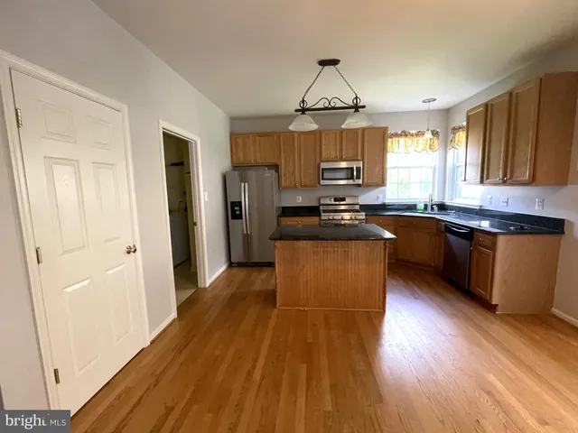 a kitchen with stainless steel appliances a microwave a stove a sink dishwasher a refrigerator and a dining table with wooden floor