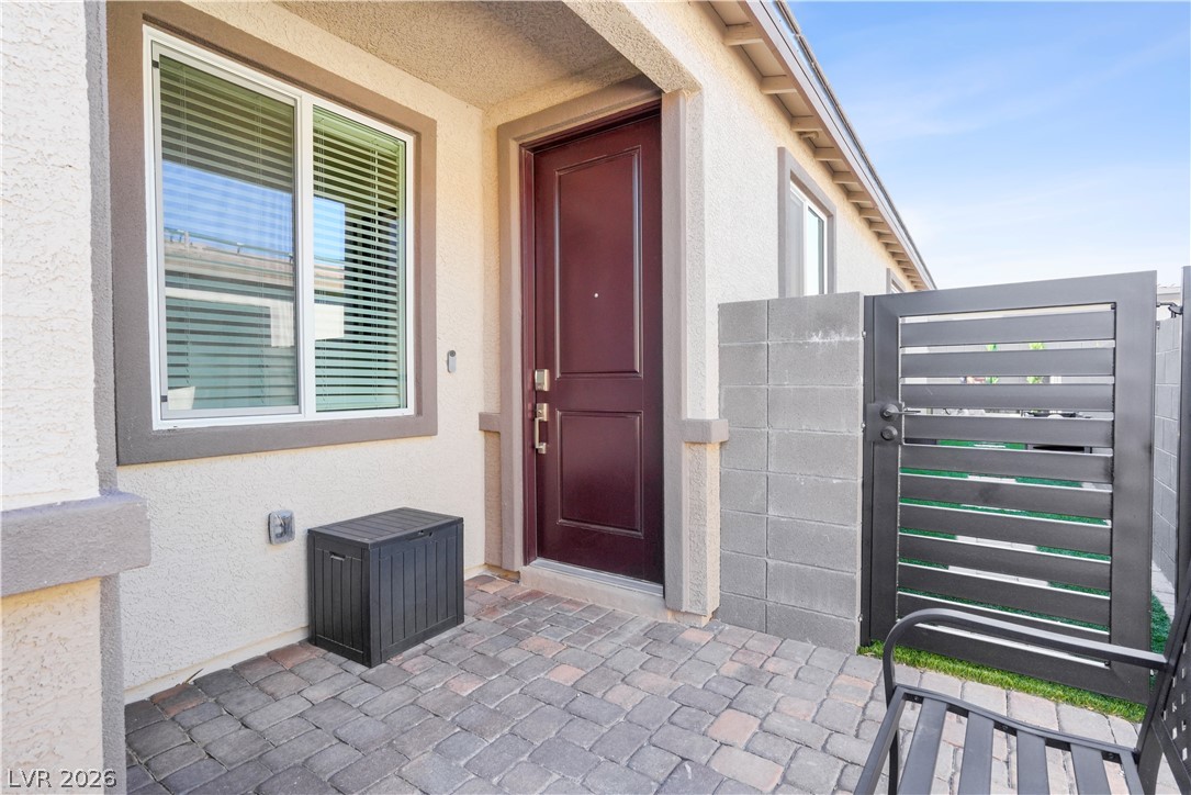 9398 Noble Fir Rdg Court Las Vegas, NV 89143 - Photo 5 of 36 A welcoming entry features a rich, dark wood door set against light stucco, framed by paver flooring and a sleek metal gate.