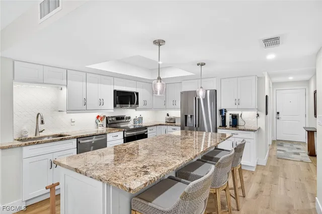 a kitchen with stainless steel appliances granite countertop a sink a stove a refrigerator a microwave oven a refrigerator with white cabinets and wooden floor