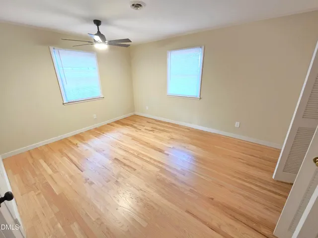 a view of an empty room with wooden floor and a ceiling fan