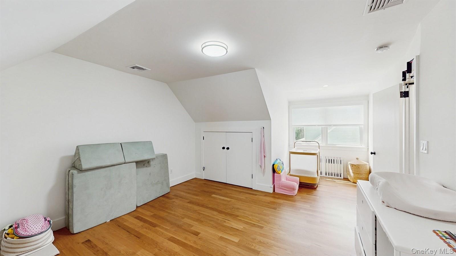 170 Wetherill Road Garden City, NY 11530 - Photo 16 of 23 Additional living space with radiator heating unit, visible vents, vaulted ceiling, and light wood-style flooring
