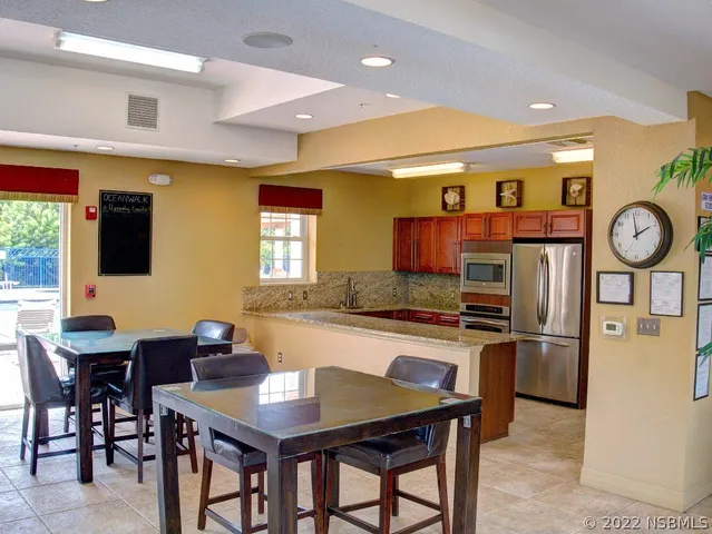 a kitchen with stainless steel appliances granite countertop a dining table chairs refrigerator and sink