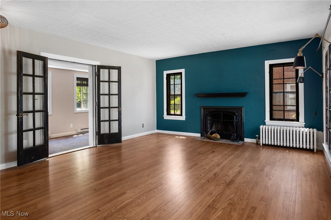 3677 Traver Road Shaker Heights, OH 44122 - Photo 4 of 35 Unfurnished living room featuring radiator, french doors, wood finished floors, a baseboard heating unit, and a textured ceiling