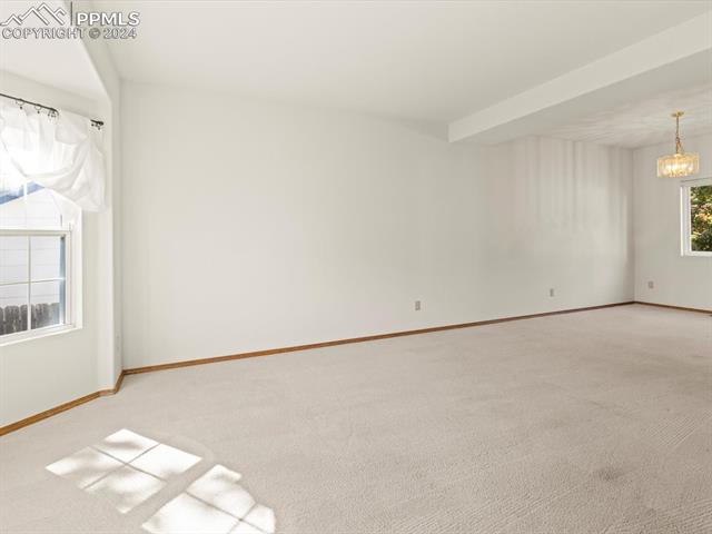 7590 Julynn Road Colorado Springs, CO 80919 - Photo 25 of 44 Empty room with light carpet and an inviting chandelier