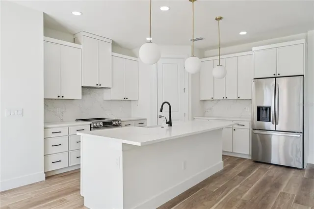 a kitchen with stainless steel appliances granite countertop a sink a stove a refrigerator and white cabinets with wooden floor