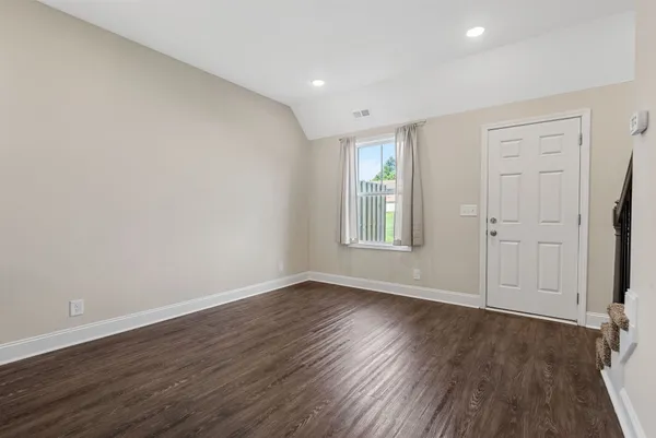 a view of an empty room with wooden floor and window