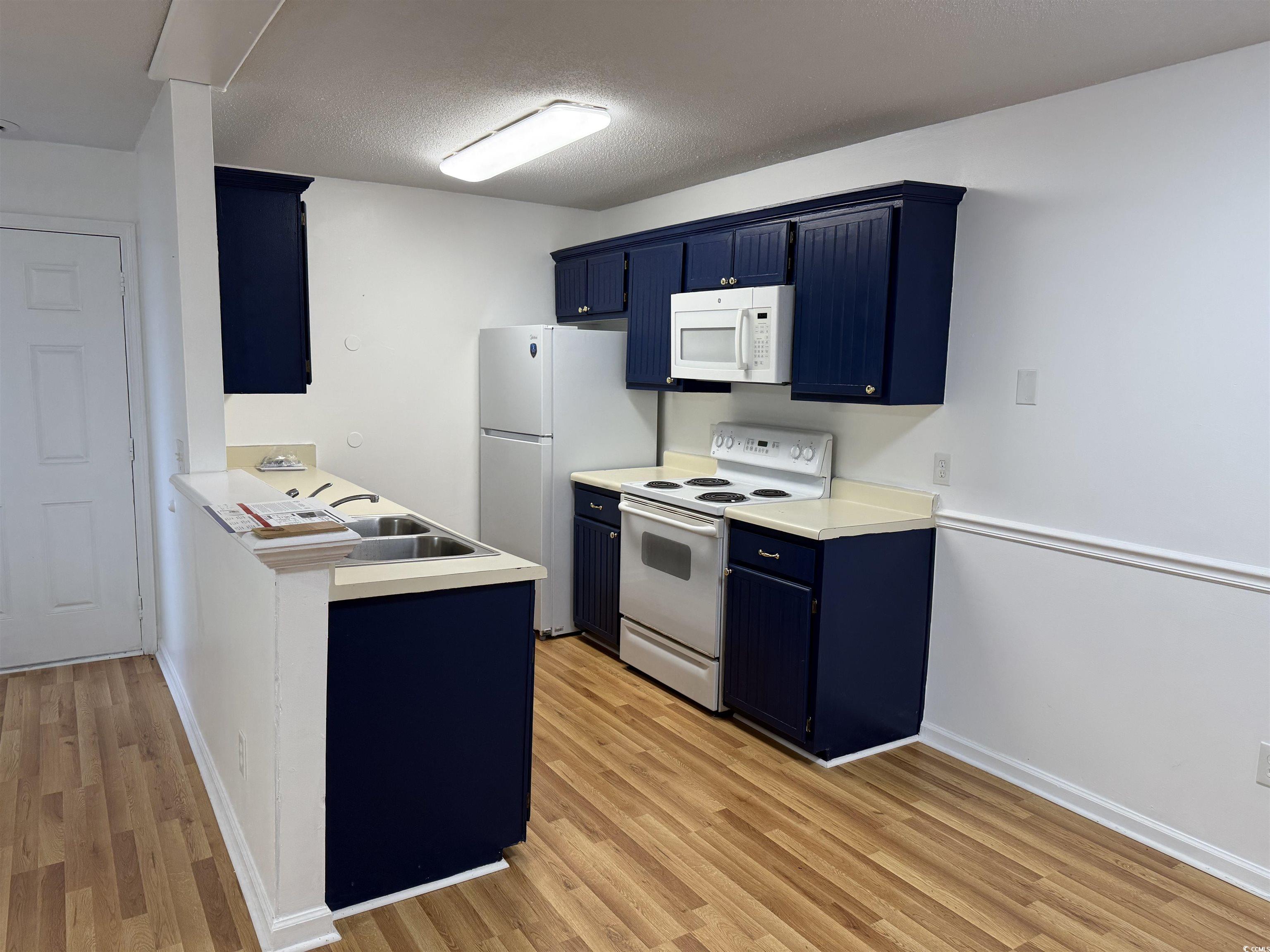 1356 Glenns Bay Road, Unit 206 Surfside Beach, SC 29575 - Photo 7 of 40 Kitchen featuring blue cabinets, white appliances, light countertops, a peninsula, and light wood-style floors