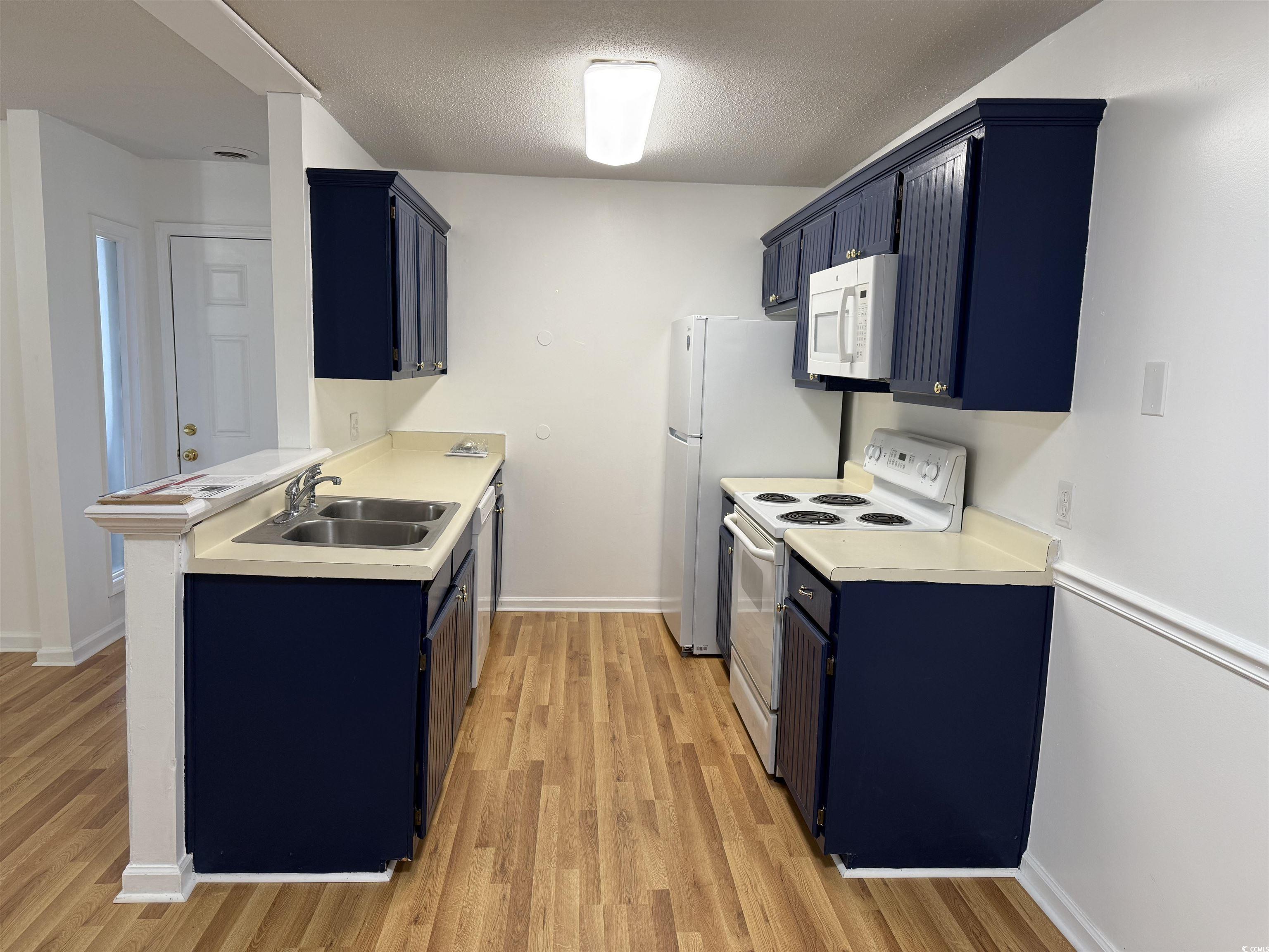 1356 Glenns Bay Road, Unit 206 Surfside Beach, SC 29575 - Photo 9 of 40 Kitchen featuring blue cabinetry, white appliances, light countertops, a textured ceiling, and light wood-style floors