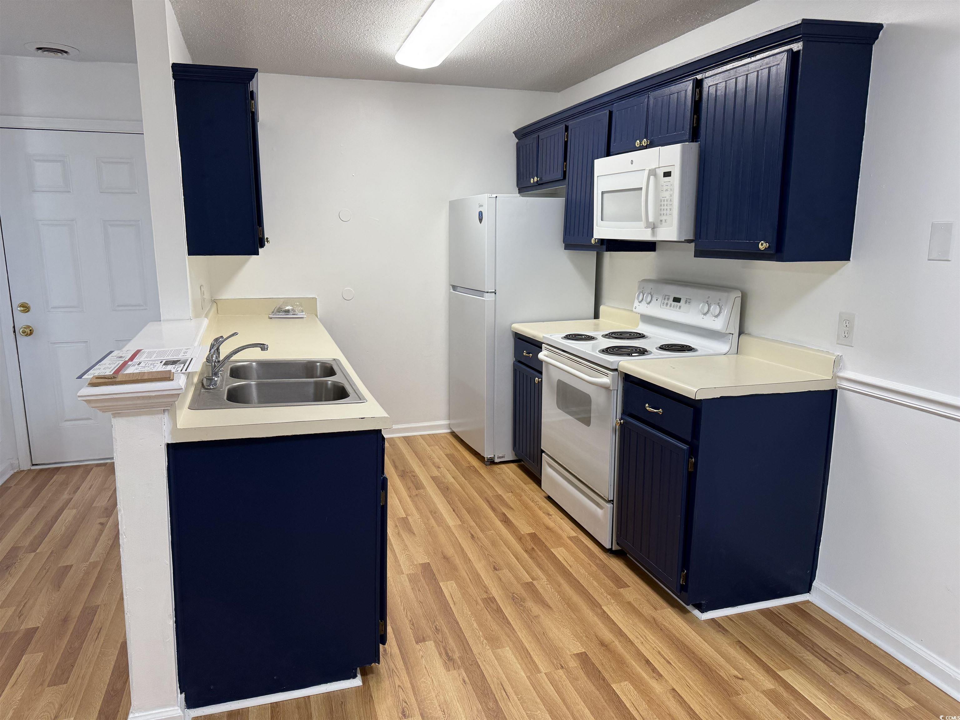 1356 Glenns Bay Road, Unit 206 Surfside Beach, SC 29575 - Photo 10 of 40 Kitchen with blue cabinets, white appliances, light countertops, light wood-type flooring, and a textured ceiling