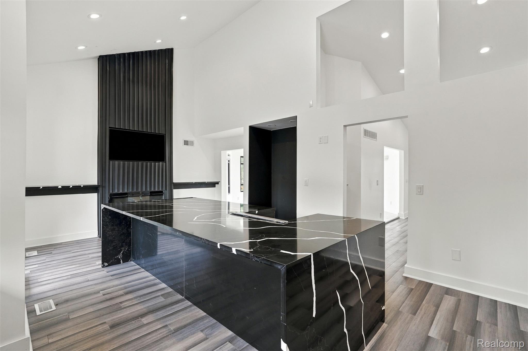 27507 Bell Road Southfield, MI 48034 - Photo 21 of 81 Modern open-concept kitchen and dining area featuring a sleek black island with waterfall countertop edge, recessed ceiling lighting, polished wood-finish flooring, white cabinetry, and floor-to-ceiling mirror paneling that enhances natural light throughout the space