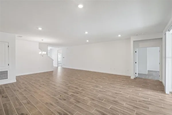 a view of an empty room with wooden floor and a kitchen