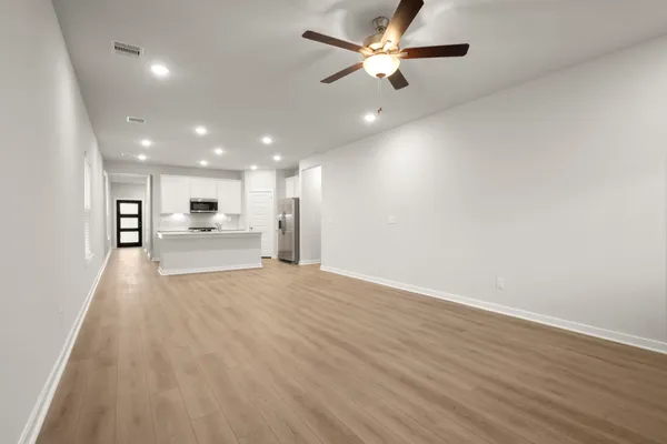 an empty room with wooden floor a ceiling fan and kitchen view