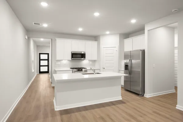 a large kitchen with stainless steel appliances granite countertop a stove a refrigerator a sink a microwave and white cabinets with wooden floor