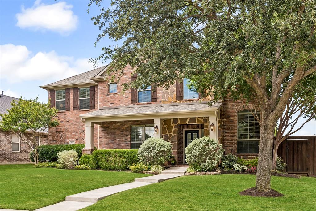960 Remuda Road Frisco, TX 75033 - Photo 38 of 39 Brick and stone facade residence featuring a covered front porch with columns, a prominent front entry, a manicured lawn, and mature trees