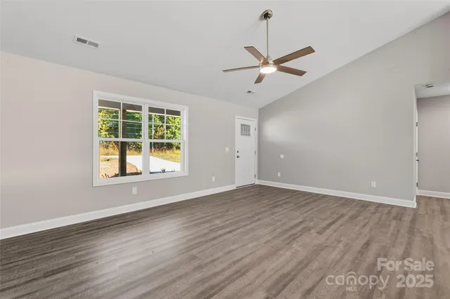 an empty room with wooden floor ceiling fan and window