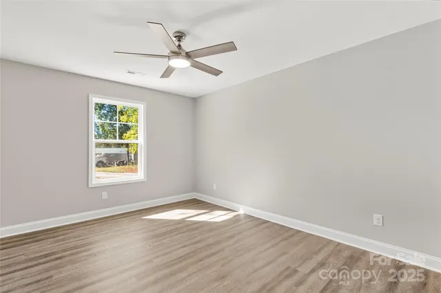 an empty room with wooden floor fan and windows