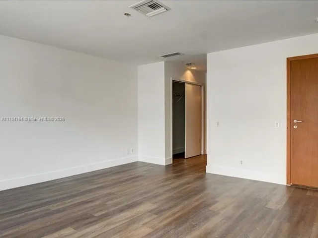 a view of an empty room with wooden floor and closet
