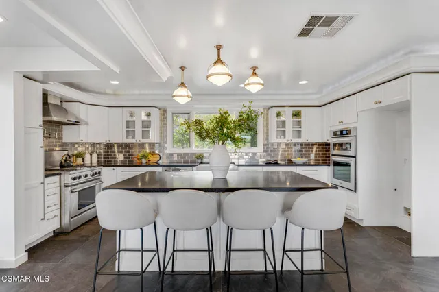 a kitchen with stainless steel appliances kitchen island granite countertop a dining table chairs and a refrigerator