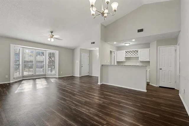a view of an empty room with wooden floor and a kitchen