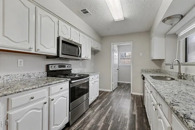 a kitchen with granite countertop a sink a stove top oven and cabinetry