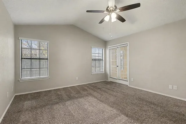 an empty room with chandelier fan and windows