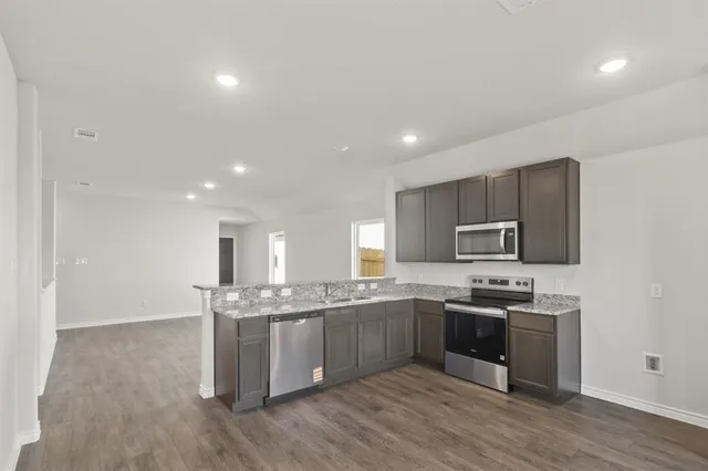 a kitchen with stainless steel appliances granite countertop a stove top oven a sink and a granite counter tops with wooden floors