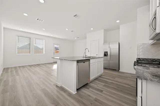 a kitchen with stainless steel appliances granite countertop a stove a sink dishwasher and a refrigerator with wooden floor