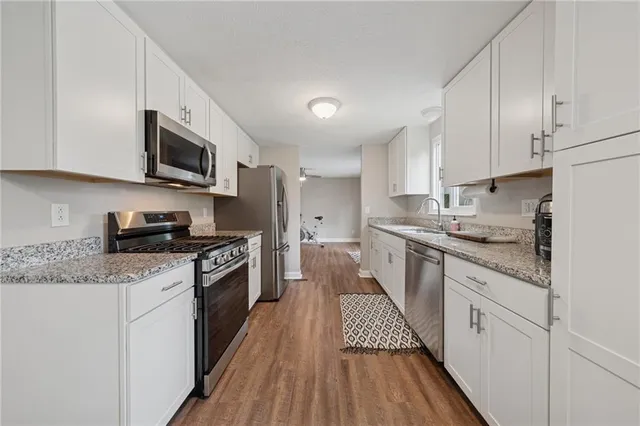 a kitchen with stainless steel appliances granite countertop a stove top oven a sink dishwasher and a refrigerator with wooden floor