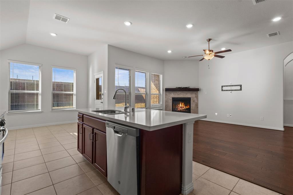 1740 Rio Costilla Road Fort Worth, TX 76131 - Photo 17 of 40 Kitchen island with a built-in sink and stainless steel appliances, tile flooring, recessed lighting, fireplace with a stone surround, and wood-finish flooring