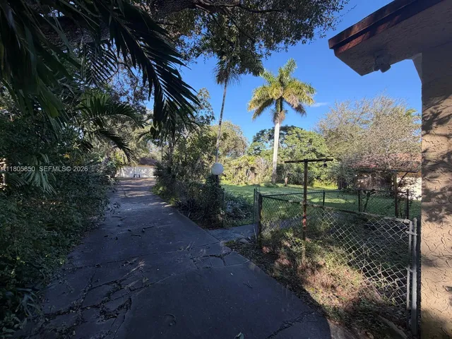 a view of a street with flower plants and large trees