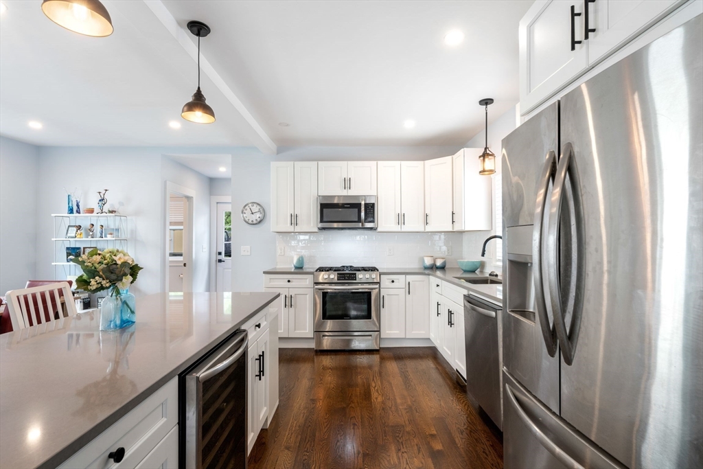 a kitchen with stainless steel appliances a stove a sink dishwasher a refrigerator white cabinets and wooden floor