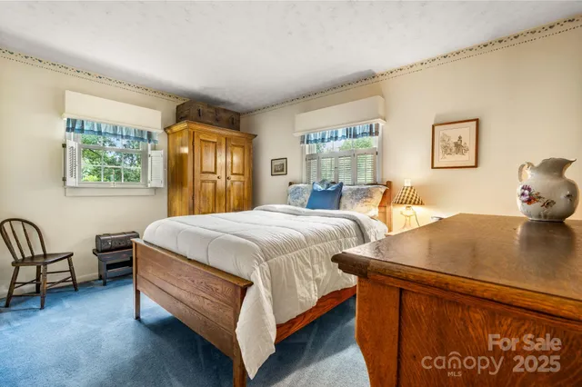 a bedroom with a bed chair and two windows