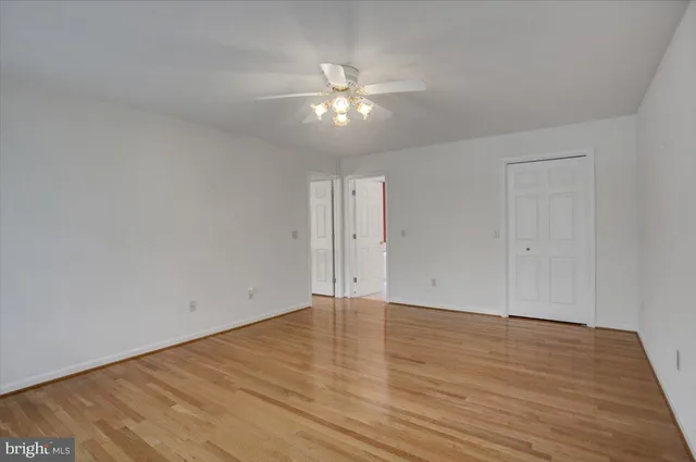 a view of an empty room with wooden floor and a ceiling fan
