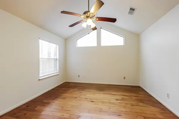a view of an empty room with wooden floor and a ceiling fan
