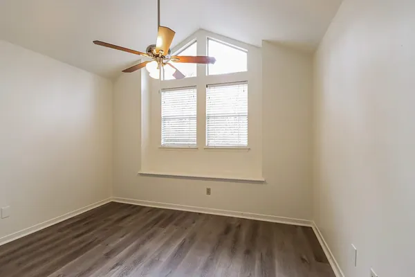 an empty room with wooden floor fan and windows