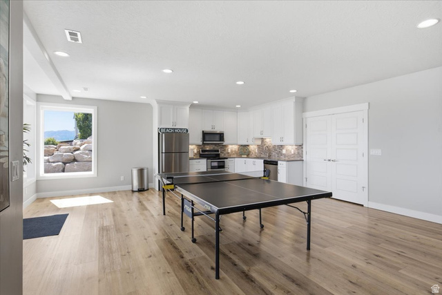 21 Pier Place Tooele, UT 84074 - Photo 53 of 112 Open-concept recreation area featuring wood-finish flooring, a full kitchen with white cabinetry and stainless steel appliances, recessed lighting, and a large window