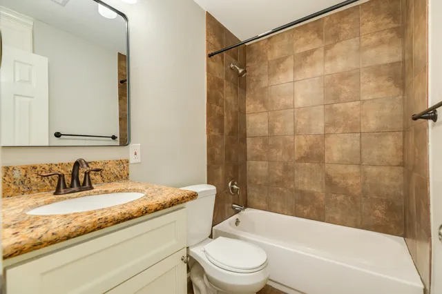 a bathroom with a granite countertop bathtub shower sink vanity mirror and toilet