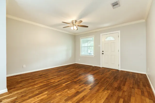 an empty room with wooden floor ceiling fan and windows