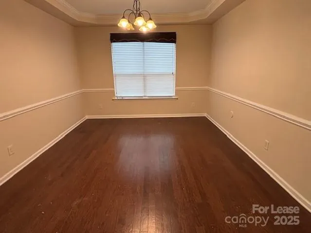 an empty room with wooden floor chandelier and windows