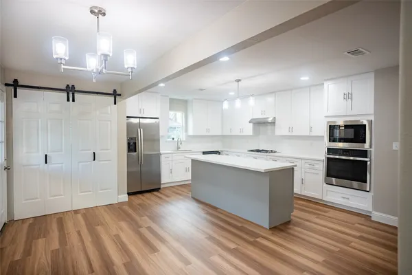 a large kitchen with a center island wooden floor stainless steel appliances and cabinets