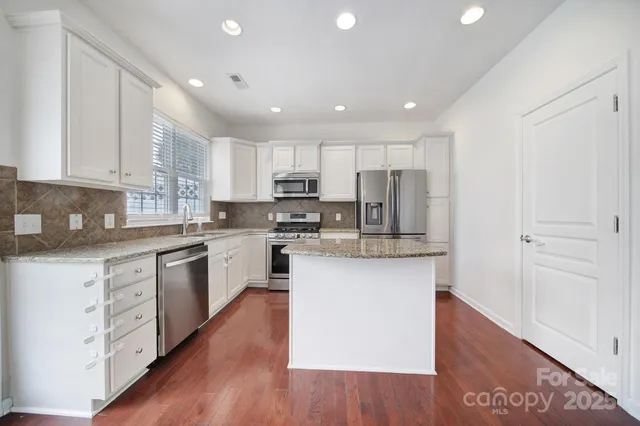 a kitchen with kitchen island granite countertop wooden floors white cabinets and stainless steel appliances