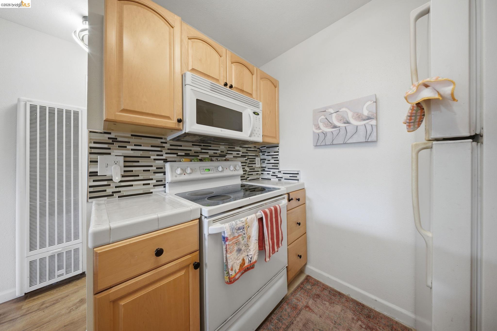 4081 Clayton Road, Unit 118 Concord, CA 94521 - Photo 8 of 30 Kitchen featuring light wood finish cabinetry, white appliances, tile countertops, a heating unit, and backsplash