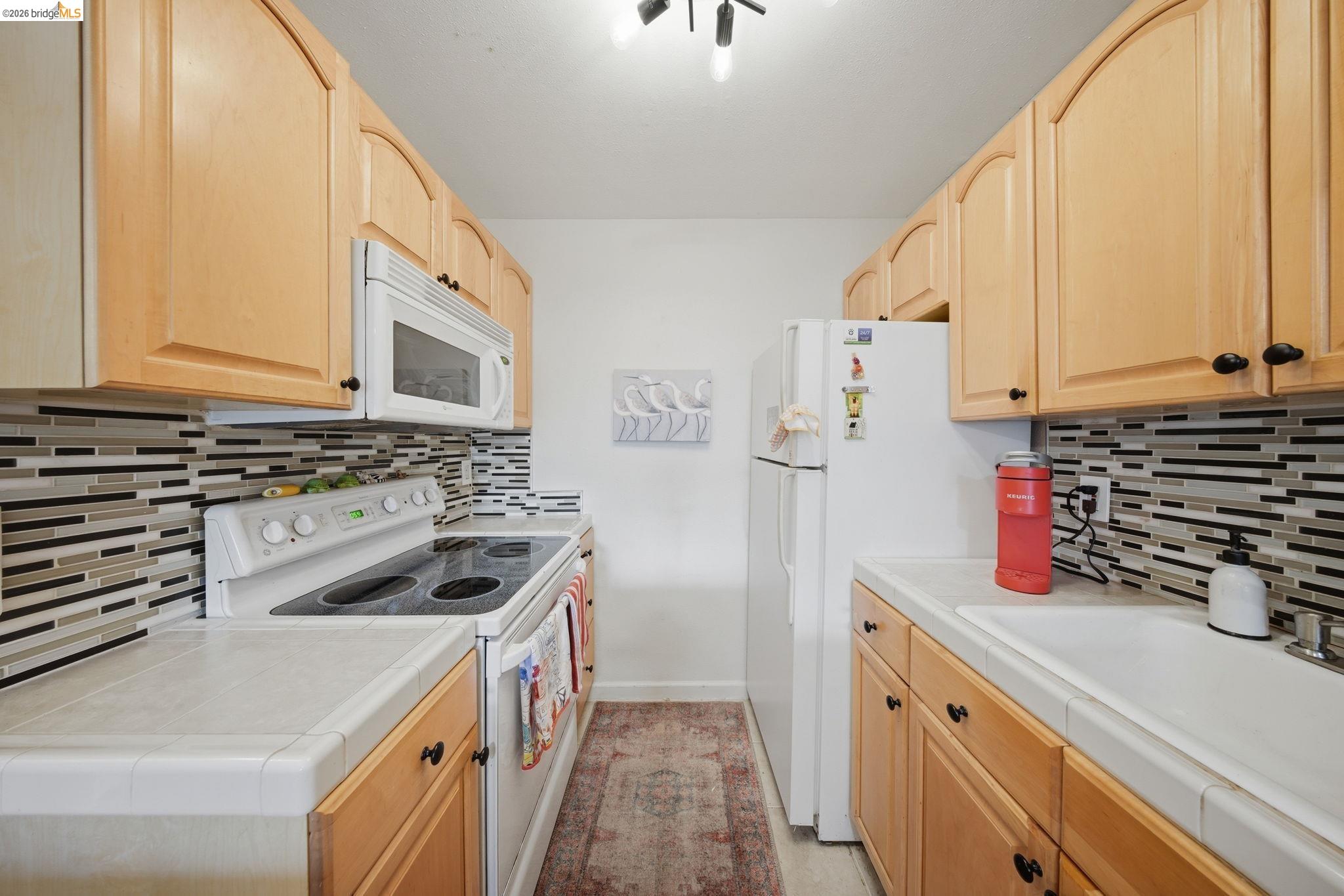 4081 Clayton Road, Unit 118 Concord, CA 94521 - Photo 9 of 30 Kitchen with light wood finish cabinetry, white appliances, and tile countertops