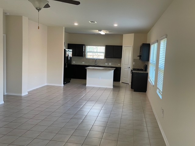 10125 Gertrudis Loop Austin, TX 78747 - Photo 27 of 27 Kitchen with dark cabinetry, a kitchen island, black appliances, open floor plan, and light tile patterned flooring