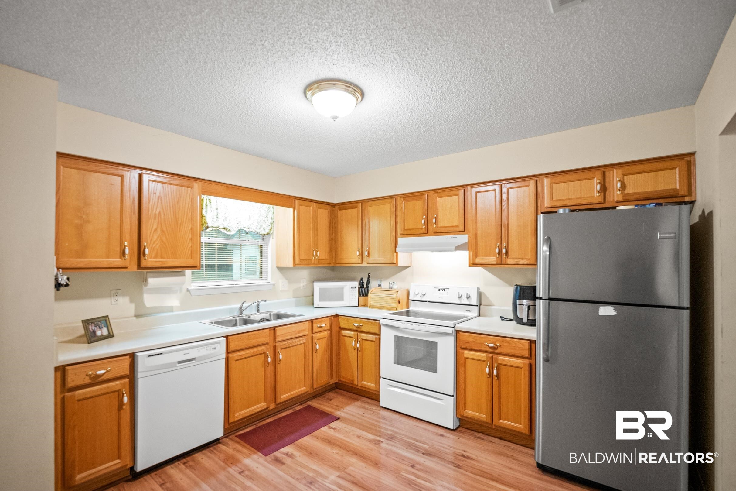 Kitchen featuring light countertops, light wood finished floors, white appliances, under cabinet range hood, and a sink