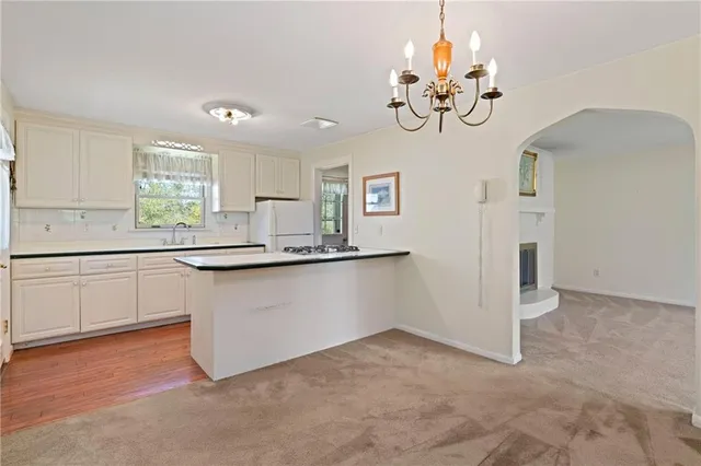 a kitchen with kitchen island granite countertop a stove a sink dishwasher and white cabinets with wooden floor