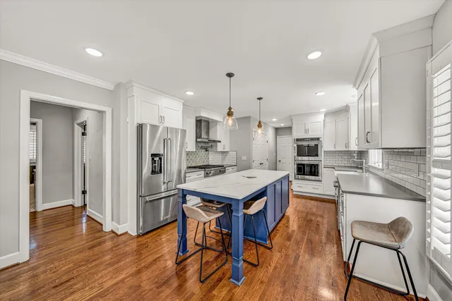 a kitchen with stainless steel appliances kitchen island granite countertop a refrigerator a stove a sink and white cabinets with wooden floor