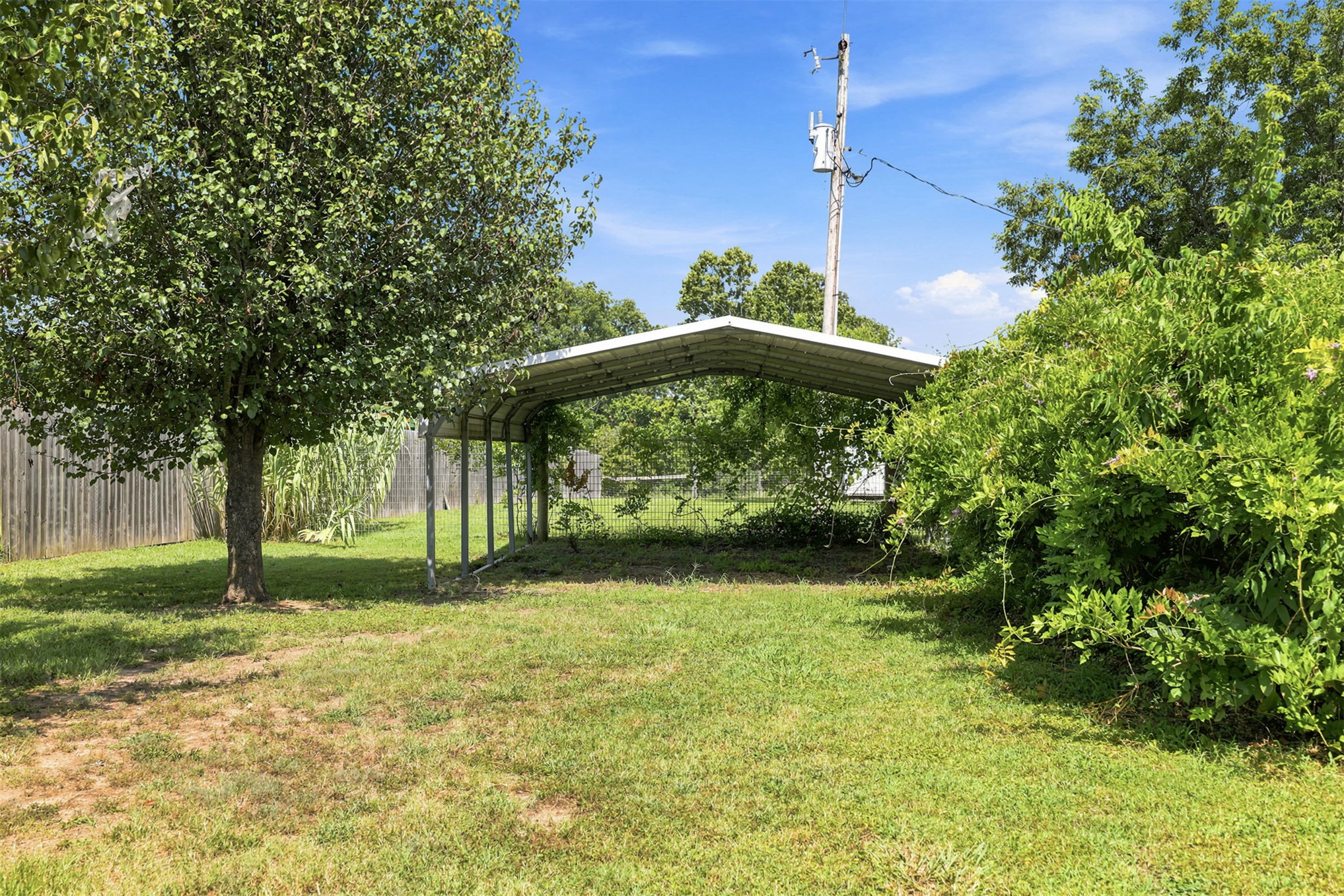 633 Swinney Road Mead, OK 73449 - Photo 24 of 32 Expansive grass area featuring a metal carport structure, mature trees, and established perimeter fencing