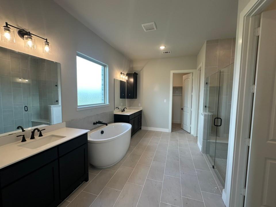 295 Brown Road Leonard, TX 75452 - Photo 15 of 28 Spacious bathroom featuring a freestanding soaking tub, dual vanity with undermount sinks, a separate glass-enclosed shower with tiled walls, and light-toned tile flooring