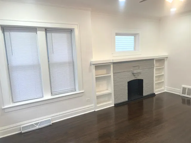 an empty room with wooden floor fireplace and windows
